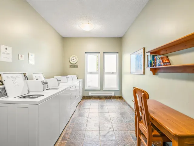 Communal laundry room featuring a textured ceiling, stone tile floors, a baseboard heating unit, and washing machine and clothes dryer