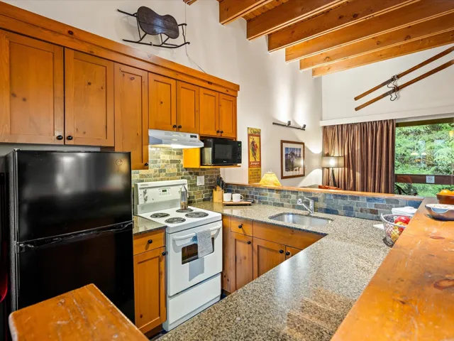 Kitchen featuring black appliances, butcher block countertops, brown cabinets, backsplash, and beamed ceiling