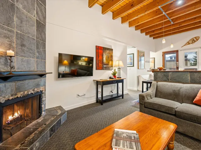 Living room featuring carpet flooring, beam ceiling, and a stone fireplace