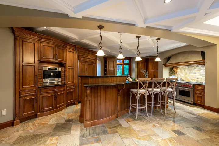 Kitchen featuring coffered ceiling, a breakfast bar, stone tile flooring, beam ceiling, and custom range hood