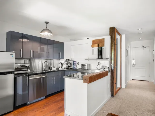 Kitchen featuring stainless steel appliances, a peninsula, modern cabinets, pendant lighting, and dark wood-style floors