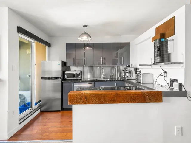 Kitchen with dark countertops, a peninsula, stainless steel appliances, pendant lighting, and dark wood-type flooring