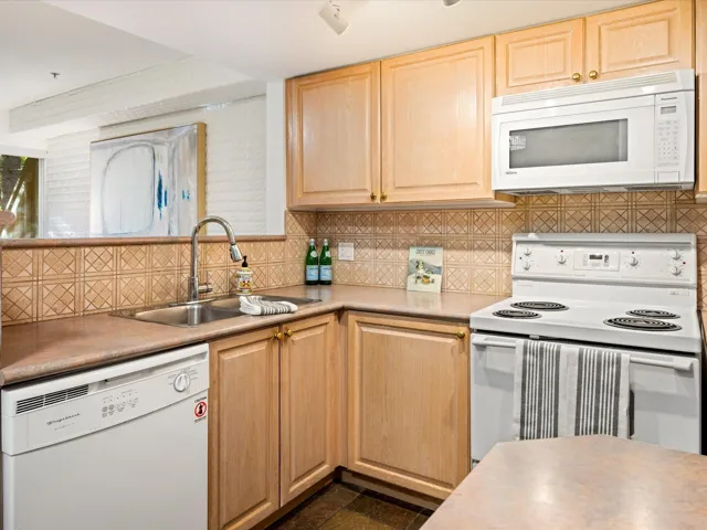 Kitchen with white appliances, light brown cabinetry, backsplash, and light countertops