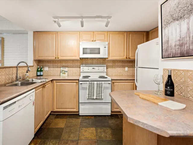 Kitchen featuring tasteful backsplash, white appliances, and light brown cabinetry