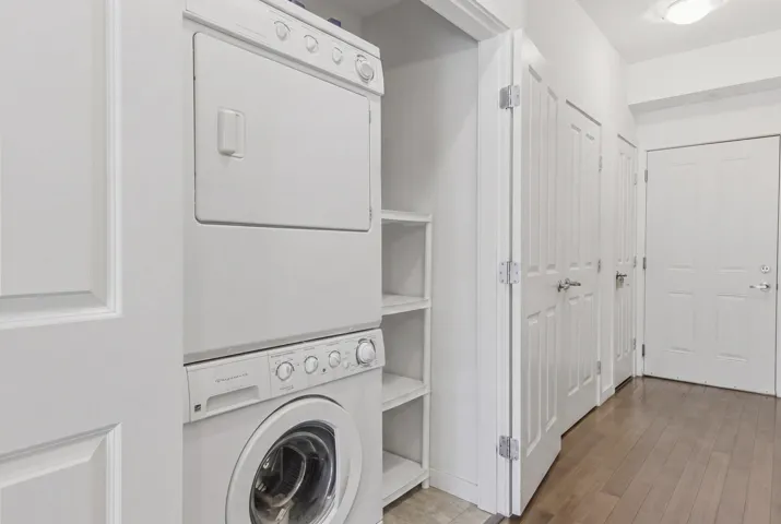 Laundry closet featuring a stacked washer and dryer unit, integrated shelving, and white paneled doors