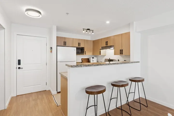 Kitchen with freestanding refrigerator, a peninsula, light wood-style floors, a breakfast bar, and light stone countertops