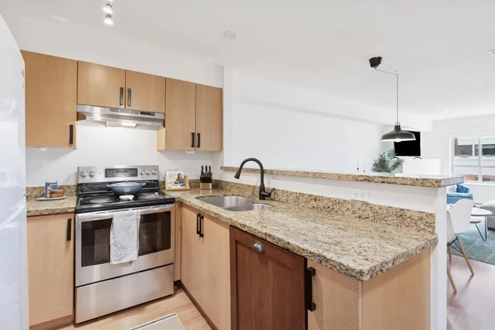 Kitchen featuring stainless steel range with electric stovetop, light stone counters, a peninsula, and pendant lighting