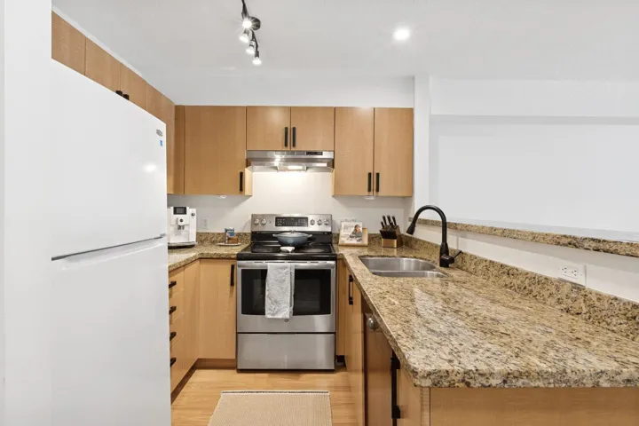 Kitchen with light stone counters, stainless steel range with electric cooktop, freestanding refrigerator, and light wood-type flooring