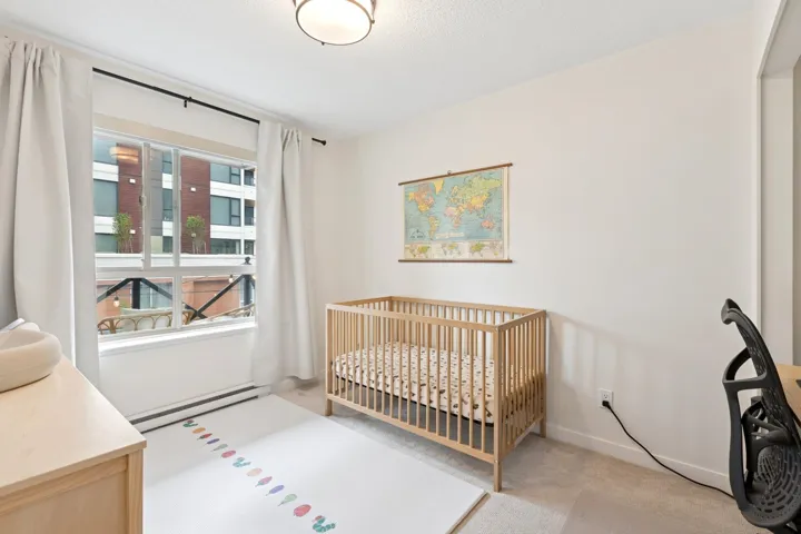 Bedroom featuring a crib, light carpet, and a baseboard heating unit
