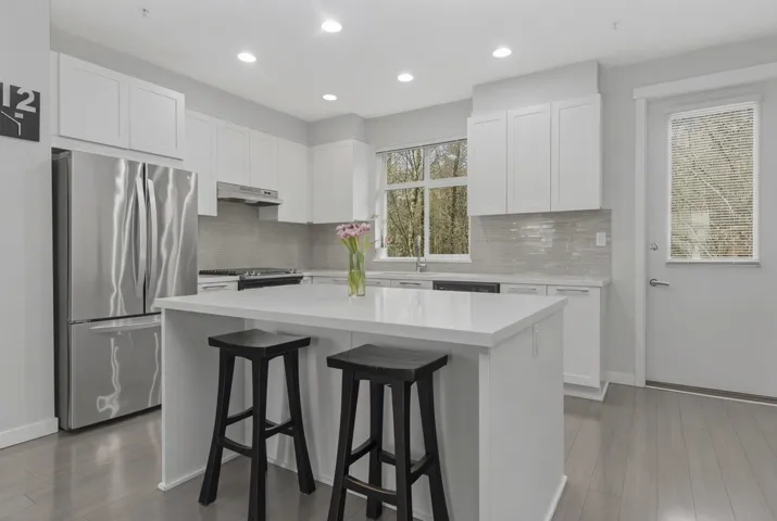 Modern kitchen featuring a central island, stainless steel appliances, white cabinetry, light-toned backsplash, and wood-finish flooring
