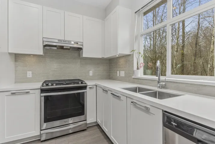 Kitchen featuring white cabinetry, light-colored countertops, stainless steel appliances, a tile backsplash, and an expansive window