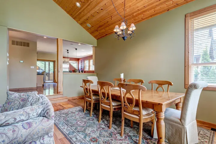 Dining room featuring visible vents, baseboards, a notable chandelier, vaulted ceiling, and wood finished floors