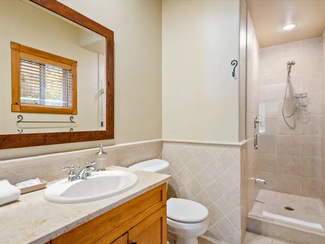 Bathroom featuring vanity, tile walls, toilet, a shower stall, and wainscoting