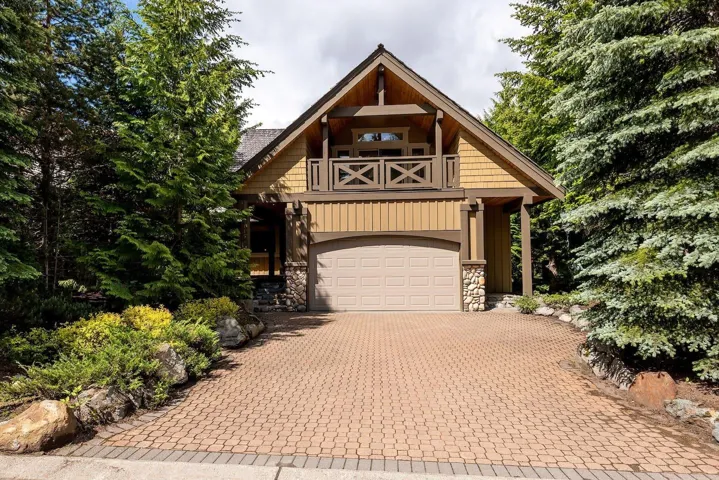 View of front of house featuring an attached garage, a balcony, stone siding, and decorative driveway