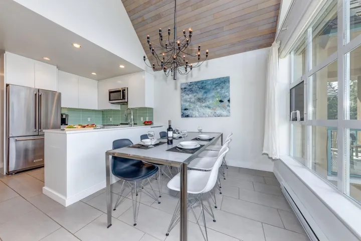 Open-concept kitchen and dining area featuring a vaulted wood-finish ceiling, stainless steel appliances, a tiled backsplash, and light-toned floor tiling