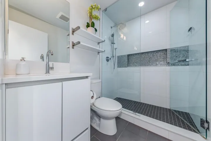 Modern bathroom featuring a frameless glass shower enclosure, white subway tile shower walls with a mosaic tile accent niche, a single-handle chrome faucet, a white vanity with integrated sink, and gray floor tiling