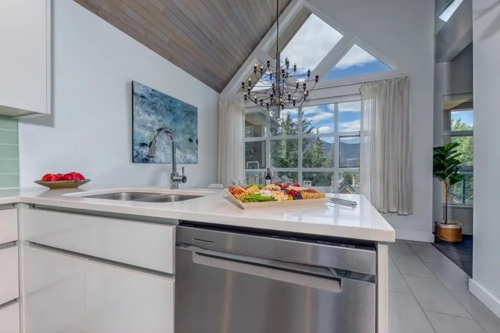 Contemporary kitchen island featuring a double stainless steel sink, a stainless steel dishwasher, and a light-toned countertop
