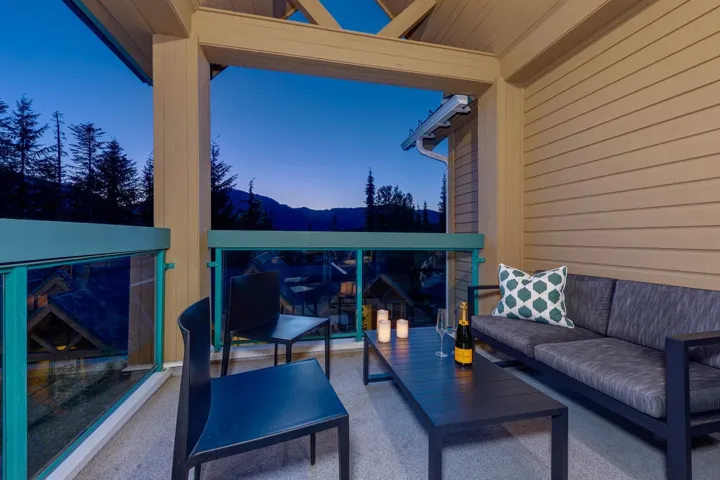 Covered outdoor balcony featuring a glass railing with teal accents, a slatted exterior wall, and a textured flooring surface