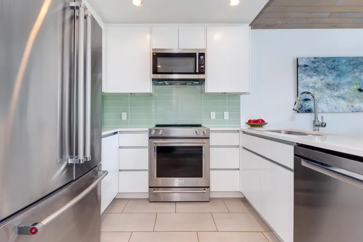 Modern kitchen featuring stainless steel appliances, white flat-panel cabinetry, a light green subway tile backsplash, light-toned flooring, and recessed lighting