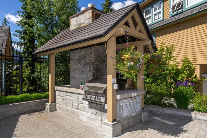 Outdoor grilling station featuring a stone-clad base, integrated stainless steel grill, and a timber-framed, shingled roof