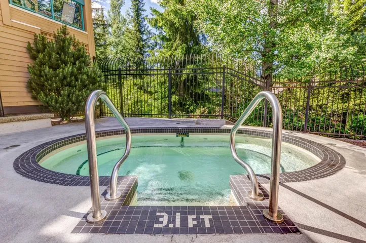 Circular hot tub featuring dark mosaic tile trim, stainless steel grab rails, and surrounding concrete decking