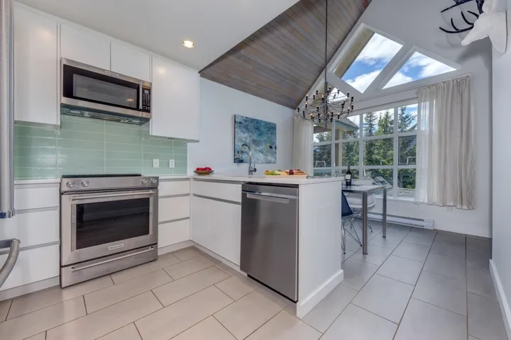 Modern kitchen featuring stainless steel appliances, white cabinetry, and a light green tile backsplash