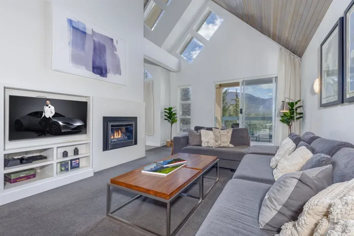 Spacious living area featuring a vaulted ceiling with wood-finish planks, a built-in media console, an integrated fireplace, and large sliding glass doors providing access to the exterior