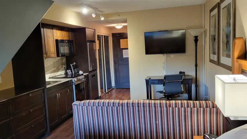 Kitchen with dark wood-style floors, backsplash, dark brown cabinets, black microwave, and stainless steel electric range
