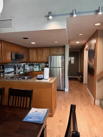 Kitchen featuring appliances with stainless steel finishes, a peninsula, brown cabinetry, light wood-style flooring, and dark stone counters