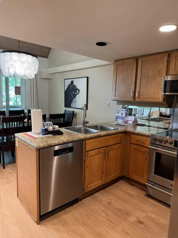 Kitchen featuring stainless steel appliances, light wood finished floors, a peninsula, brown cabinetry, and recessed lighting