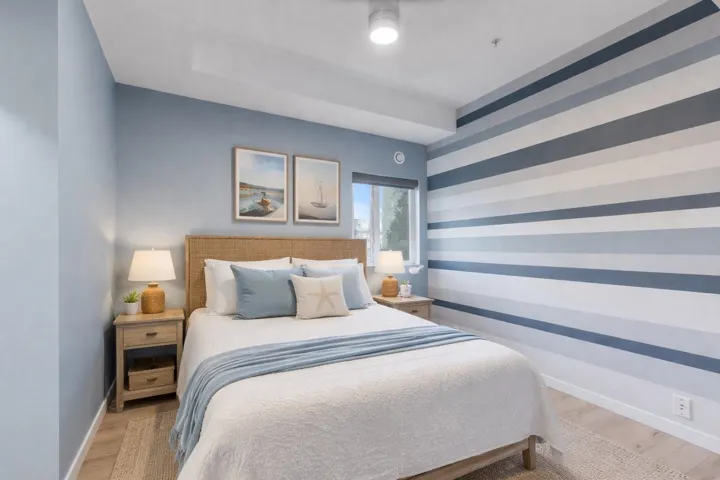 Bedroom with an accent wall, wood finished floors, and wallpapered walls. Please note this photos is virtually staged.