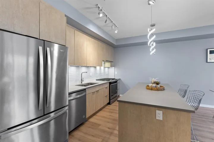 Kitchen with appliances with stainless steel finishes, a breakfast bar area, light brown cabinets, backsplash, and decorative light fixtures