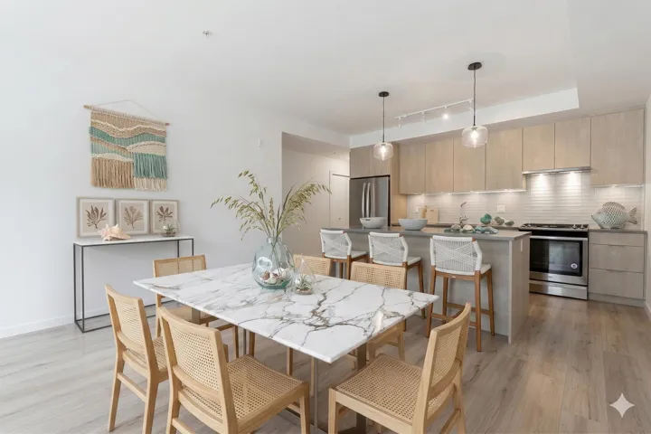 Kitchen with a breakfast bar area, light brown cabinetry, modern cabinets, and appliances with stainless steel finishes. Virtually staged with different light fixtures.
