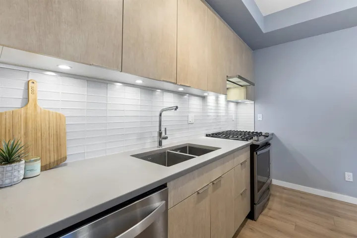 Kitchen with stainless steel appliances, modern cabinets, light wood-style floors, and light stone counters