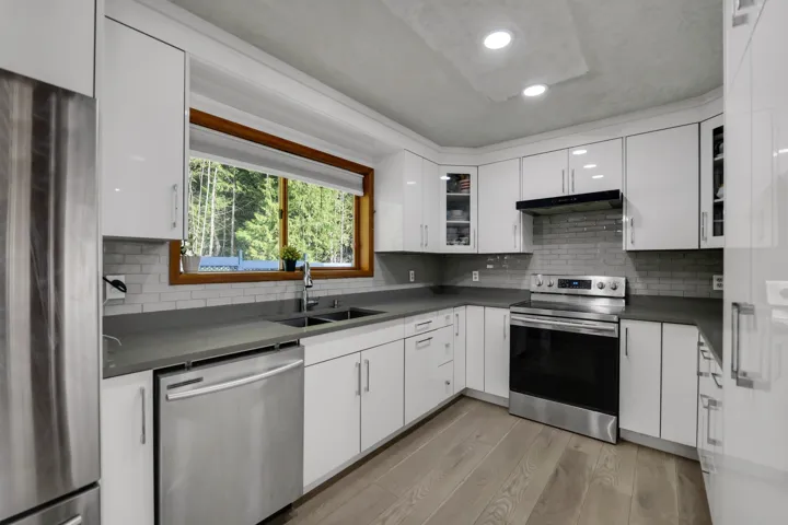 Kitchen featuring stainless steel appliances, dark countertops, light wood-style floors, white cabinetry, and recessed lighting