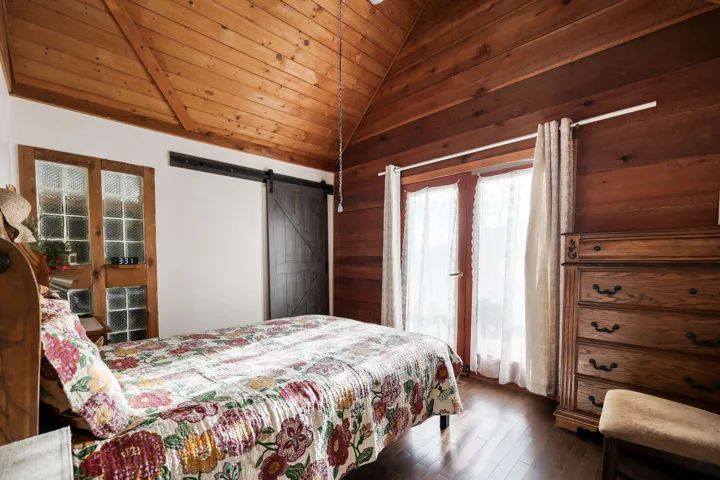 Bedroom with a barn door, a vaulted wood ceiling, dark wood finished floors, and wooden walls