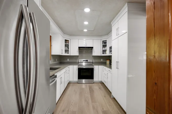 Kitchen with stainless steel appliances, white cabinetry, light wood-style flooring, tasteful backsplash, and recessed lighting