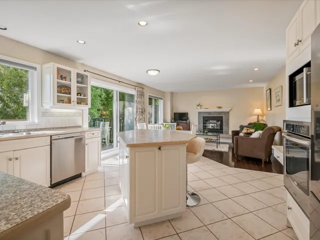 Kitchen featuring a glass covered fireplace, a center island, appliances with stainless steel finishes, light tile patterned flooring, and glass insert cabinets