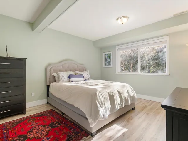 Bedroom featuring beam ceiling, light wood-style flooring, visible vents, and baseboards