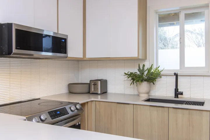 Kitchen featuring decorative backsplash, stainless steel appliances, light countertops, white cabinets, and modern cabinets