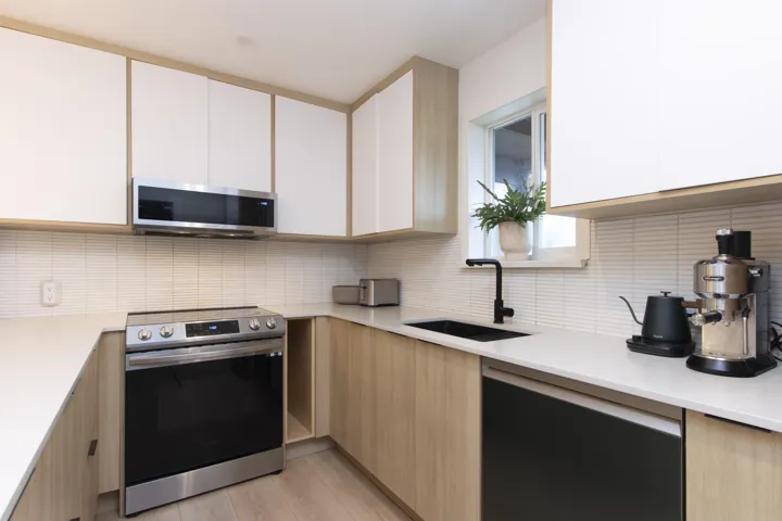 Kitchen with stainless steel appliances, two tone color scheme, modern cabinets, tasteful backsplash, and light wood-type flooring