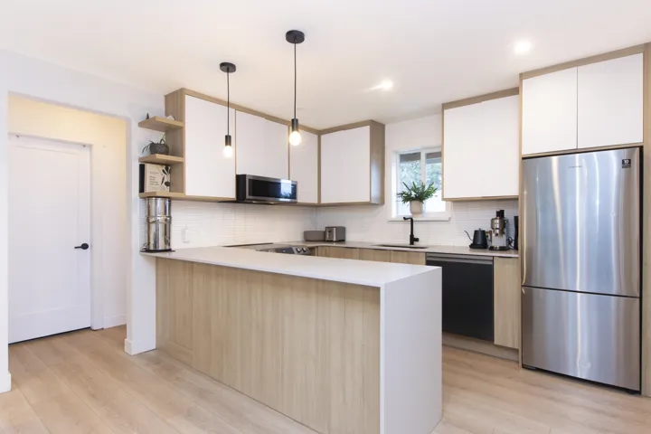 Two tone kitchen featuring a peninsula, stainless steel appliances, open shelves, dual tone cabinetry, and decorative light fixtures