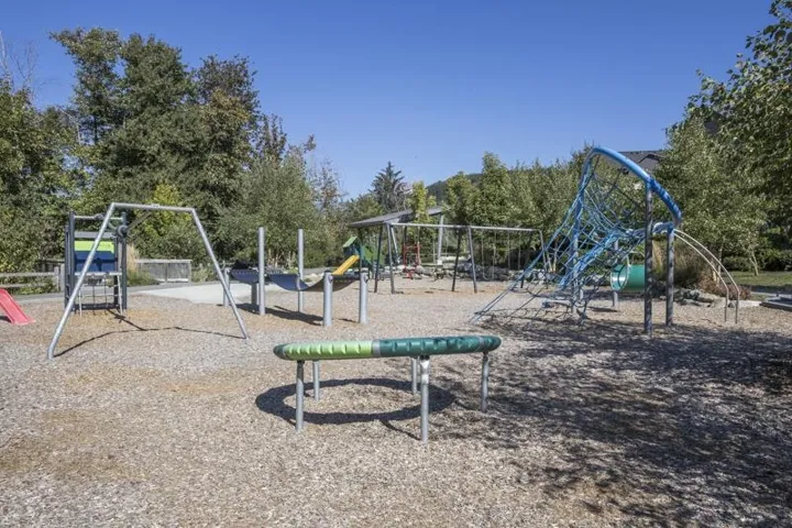 Expansive outdoor play area featuring multiple recreational structures, integrated slides, swing sets, a climbing net, and natural wood chip surfacing