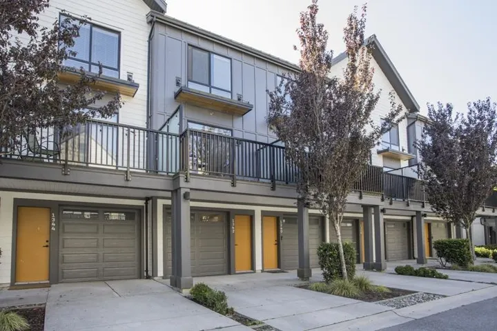 Contemporary multi-level townhome architecture featuring individual garages, private balconies with metal railings, and contrasting exterior finishes
