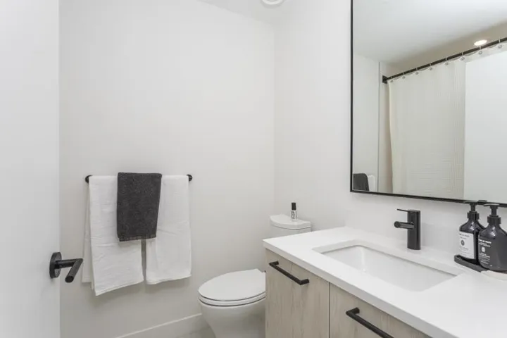 Modern bathroom featuring a wood-finish vanity with a light countertop, integrated sink, and matte black faucet