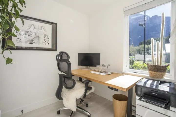 Light-toned wood-finish flooring, a large window with roller shades, and a wood-finish desk