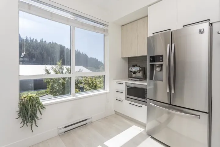 Full-height windows, stainless steel appliances, wood-finish flooring, white cabinetry with dark hardware, and a tiled backsplash