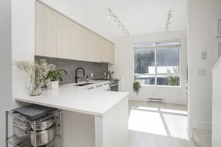 Modern kitchen featuring light wood-finish cabinetry, white countertop, and a dark tile backsplash