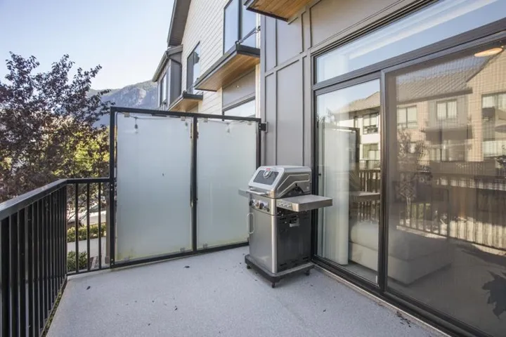 Private balcony with a dark metal railing, frosted privacy screens, and a large sliding glass door