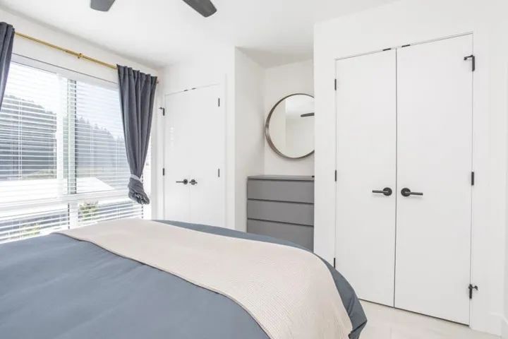 Full-height windows with blinds, white doors with matte black hardware, and a ceiling fan